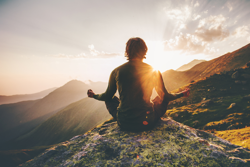 individual performing mindfulness meditation on mountain