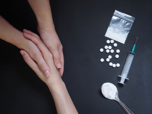 Holding hands for helping drug addict teenage on black table with drug powder syringe and pills.