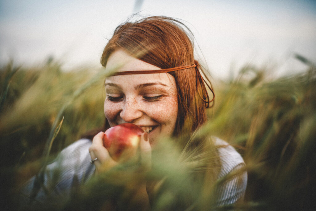 woman in addiction recovery practicing good nutrition by eating apple in green field