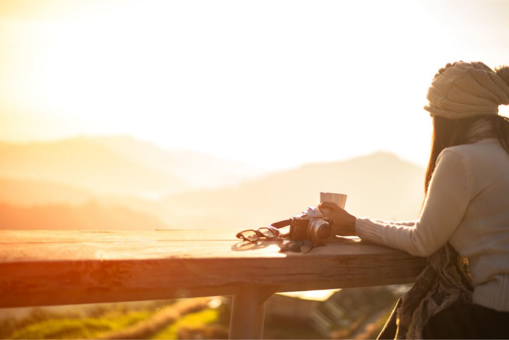 An inspiring image of a woman standing outdoors, looking at a vibrant sunset over a serene landscape. She appears contemplative and hopeful, symbolizing strength and renewal in her journey of recovery from substance use disorders.