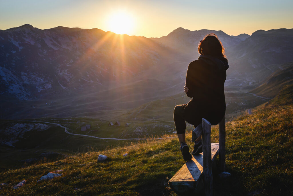 Silhouette of a woman standing triumphantly on a mountain top at sunset, symbolizing strength, resilience, and the journey of recovery.