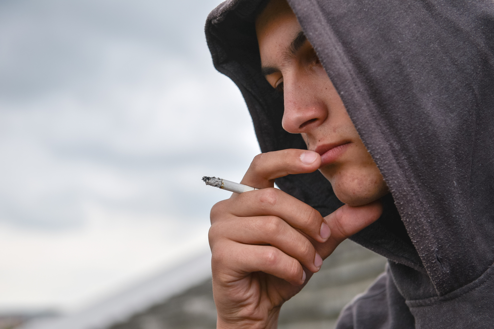 Young man smoking a cigarette contemplating social detox and rehab treatment for addition.