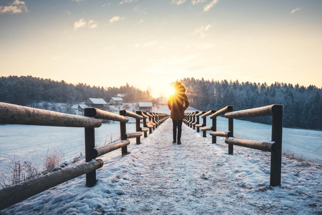 Person walking along a snowy path in a peaceful winter landscape, symbolizing strength and resilience in recovery during the holidays.